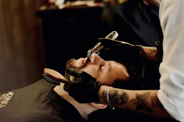 Un coiffeur rase un client au rasoir.